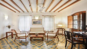 A room with a wooden ceiling, a patterned floor, a dining table with chairs, a sofa set, and a painting on the wall.