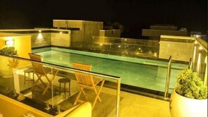 A rooftop pool area with glass balustrades, seating, and potted plants.