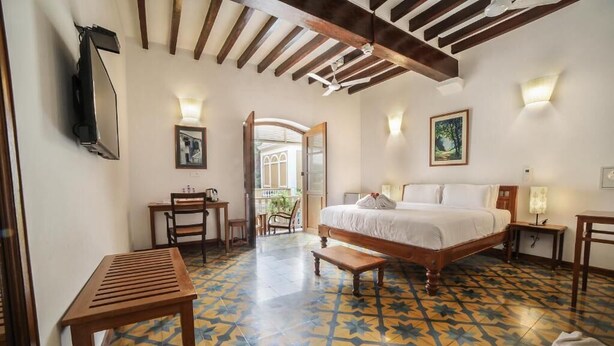 A bedroom with a bed, a desk, a chair, a wooden table, and a patterned floor.