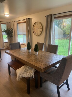 Comedor con mesa de madera, cuatro sillas, un reloj y vista al patio trasero.