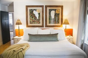 Ein Hotelzimmer mit einem Bett, zwei Nachttischen, zwei Lampen und zwei gerahmten Kunstwerken an der Wand.