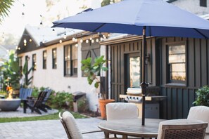 Eine Terrasse im Freien mit einem runden Tisch und Stühlen, einem blauen Sonnenschirm und Lichterketten.