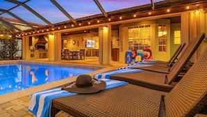 An outdoor pool area with lounge chairs, a barbecue grill, and a covered patio.