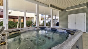 Un jacuzzi con revestimiento de piedra, rodeado de un porche cubierto con pilares blancos.