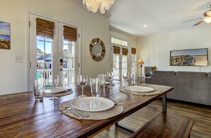 Un coin repas avec une table en bois dressée pour quatre personnes, un miroir rond et une vue sur la plage par les fenêtres.