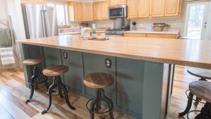 A spacious kitchen with wooden cabinets, a large island with stools, stainless steel appliances, and a view to the outside. - Dogs welcome - Gorgeous, Spacious Cabin in the Pines (Heber)