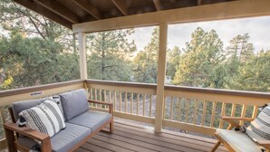 A wooden deck with a sofa and a chair, a railing, and a view of trees. - Dogs welcome - Gorgeous, Spacious Cabin in the Pines (Heber)