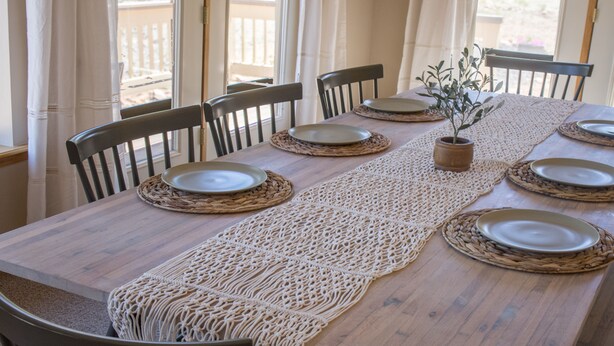 A wooden dining table with woven placemats, six chairs, and a potted plant. - Dogs welcome - Gorgeous, Spacious Cabin in the Pines (Heber)
