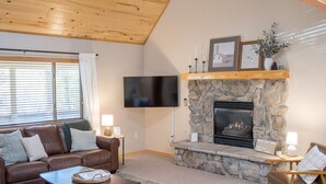 A cozy living room with a stone fireplace, leather sofa, and a flat-screen TV. - Dogs welcome - Gorgeous, Spacious Cabin in the Pines (Heber)