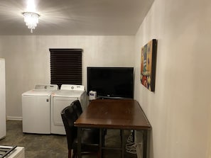 A compact room with a washing machine, a flat-screen TV, a dining table, and a chair. - Antique/Vintage Style Ranch House (Atlanta)