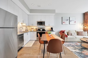A modern kitchen with white cabinets, stainless steel appliances, and a dining area with a wooden table and chairs.