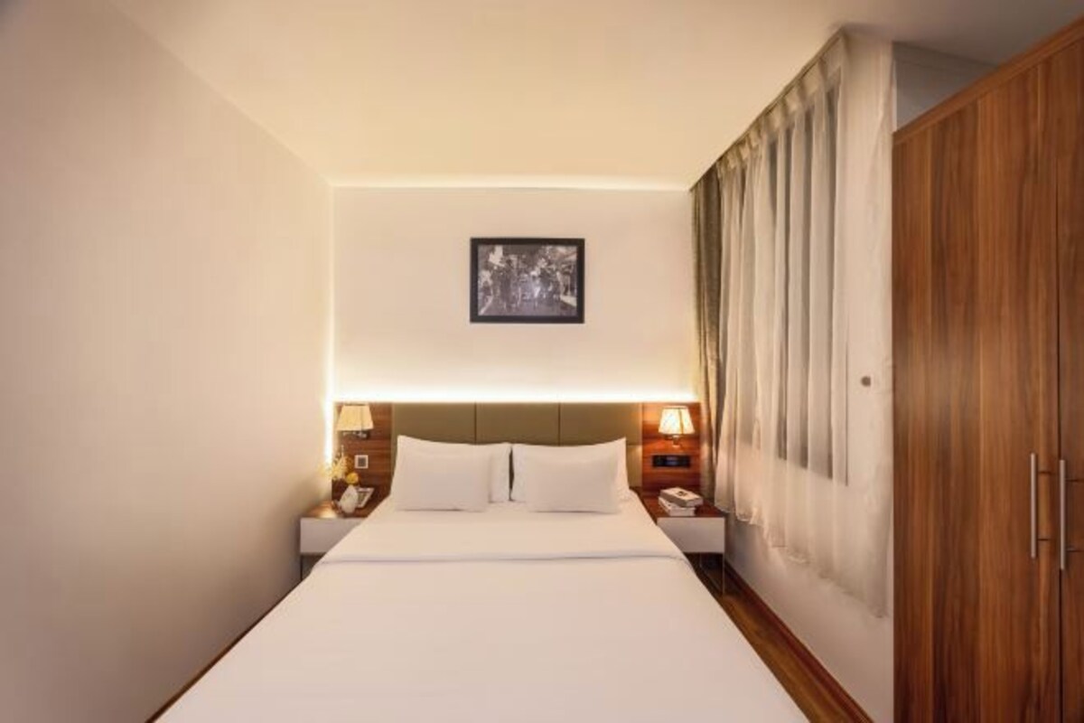 A hotel room with a large bed, two bedside tables with lamps, a wooden wardrobe, and a framed picture on the wall.