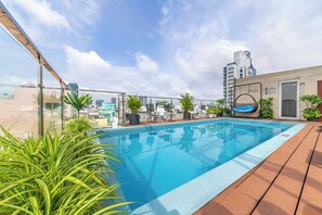 Ein Dachpool mit klarem, blauem Wasser, umgeben von Topfpflanzen und Liegestühlen.