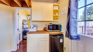 A compact kitchen with white cabinetry, a stainless steel refrigerator, a microwave, and a wooden countertop.