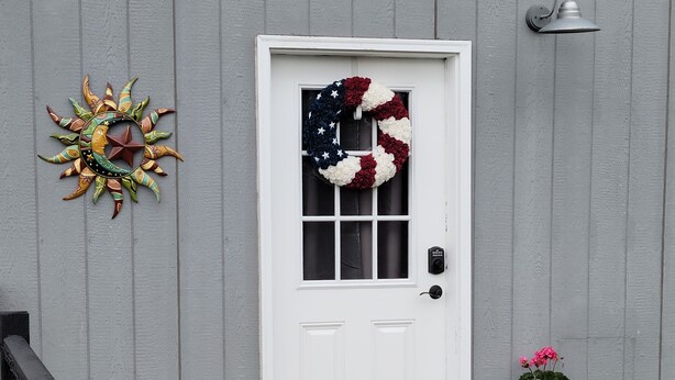A white door with a wreath, a wall-mounted light, and a potted plant.