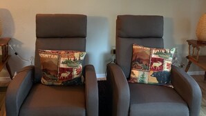 Twee bruine fauteuils met gekleurde kussens, een houten wandklok en een zeshoekige spiegel.