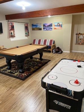 A pool table with a wooden floor, a foosball table, and a sofa with patterned cushions.