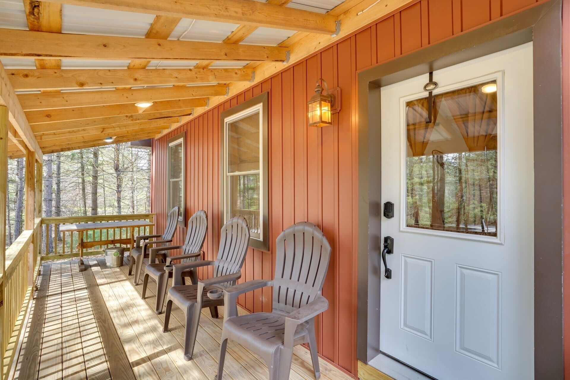 Eine hölzerne Veranda mit Adirondack-Stühlen, einer weißen Tür und Blick auf den Wald.