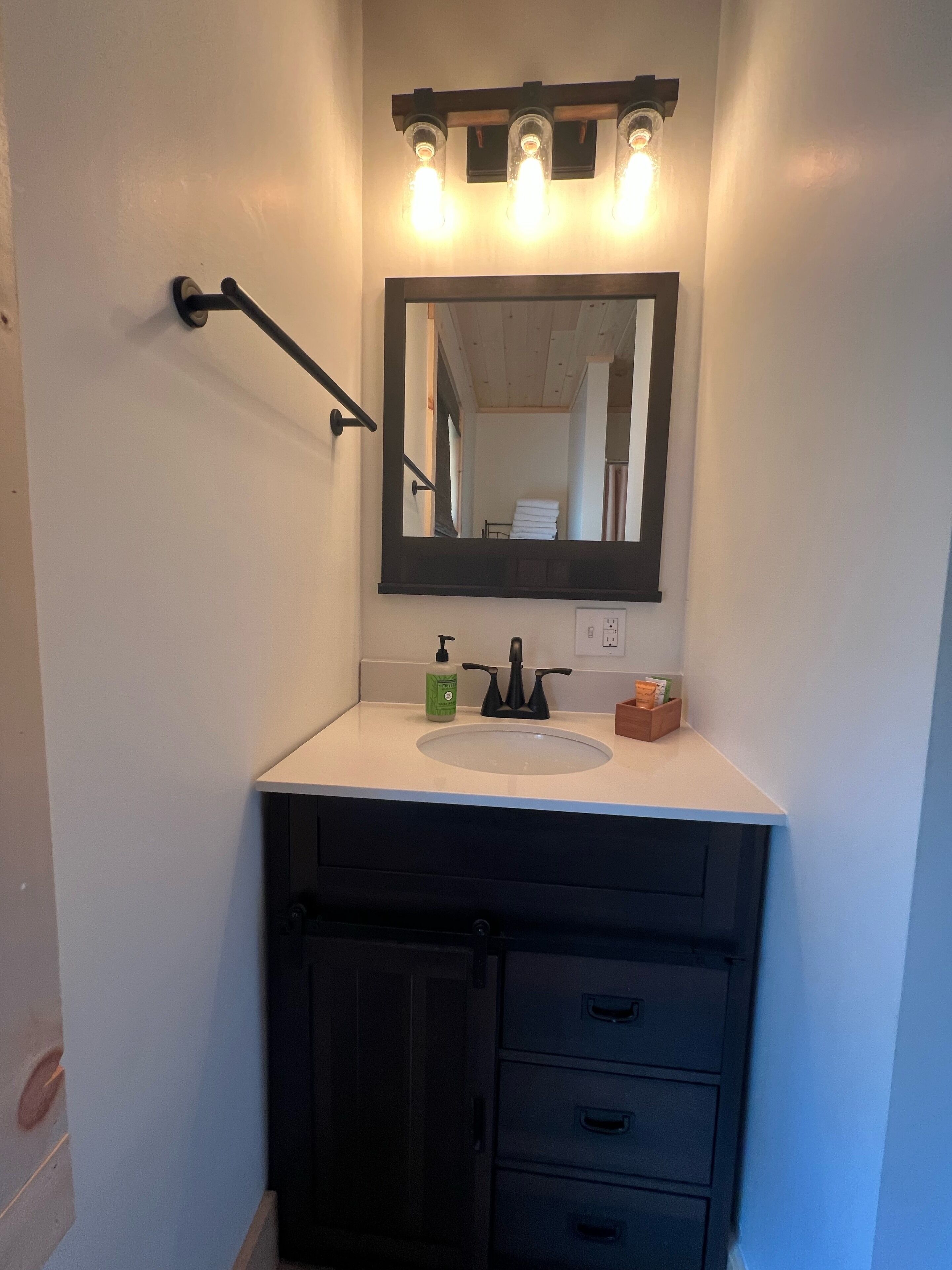 Une salle de bain avec un lavabo blanc, un meuble noir et un miroir surmonté de trois ampoules.