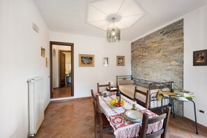 Un coin repas avec une table dressée pour deux personnes, un mur en pierre et une vue sur une autre pièce.