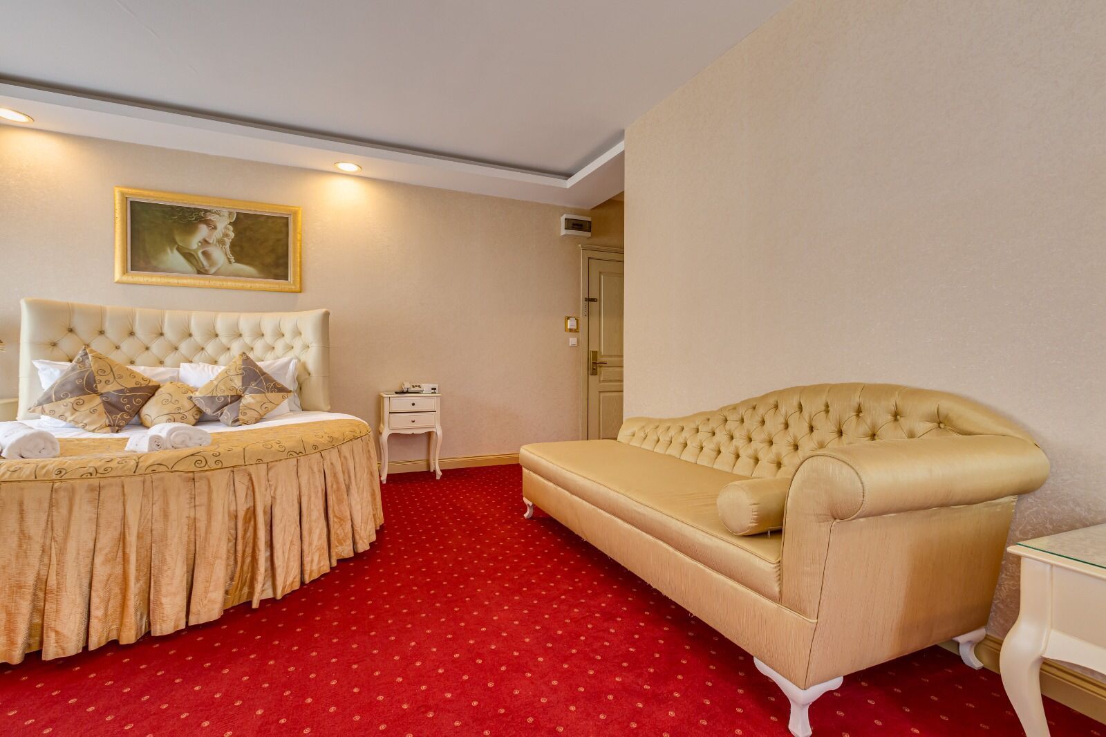 A hotel room with a large bed, a sofa, a small table, and a painting on the wall.