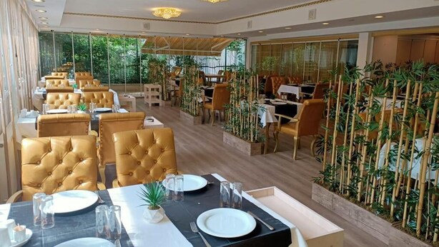 Un restaurante con sillas de cuero de respaldo alto, mesas redondas y una pared decorada con plantas de bambú.