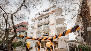 Entrada de un hotel con alfombra roja, arcos de globos negros y anaranjados, y un letrero que dice "Wins Boutique Hotel".