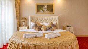 Habitación de hotel con una cama grande, cabecera, un cuadro, una mesita de noche, una lámpara y una alfombra roja.