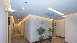 Een hotelgang met vloerbedekking, potplanten en een bordje dat de richting naar de lift aangeeft.