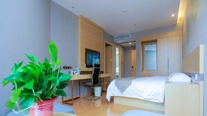 Een moderne hotelkamer met een bed, bureau, stoel, televisie en een potplant.