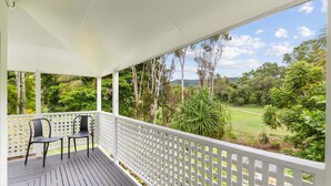 A covered porch with a view of a lush green landscape and a golf course.