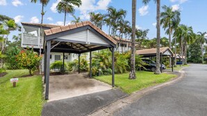 A residential property with a covered driveway, palm trees, and a sign indicating no parking.