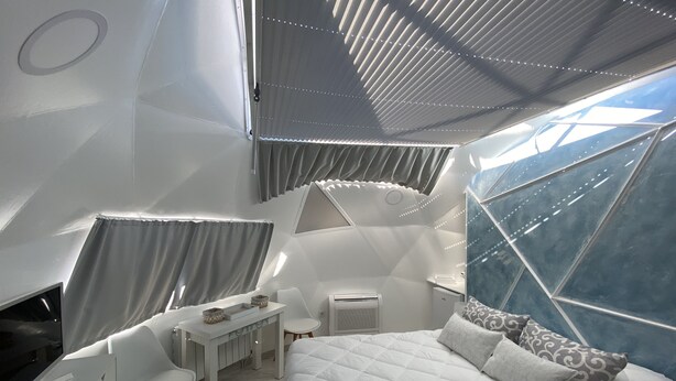 Un dormitorio moderno de diseño geométrico con cama, escritorio y sillas, que cuenta con un ventanal grande y un plafón con una lámpara original.