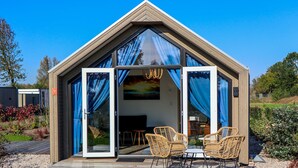 A modern, triangular-roofed structure with glass doors and windows, featuring wicker furniture and a chandelier. - Europarcs Marina Strandbad (Olburgen)