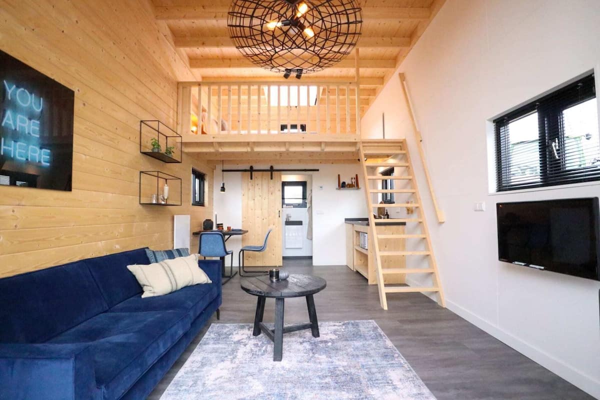 Un intérieur moderne avec un canapé bleu, une petite table ronde, un plafond en bois et un escalier.