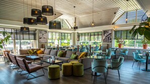 A spacious indoor area with a high ceiling, large windows, and a variety of seating arrangements including sofas, chairs, and ottomans. - Europarcs Marina Strandbad (Olburgen)