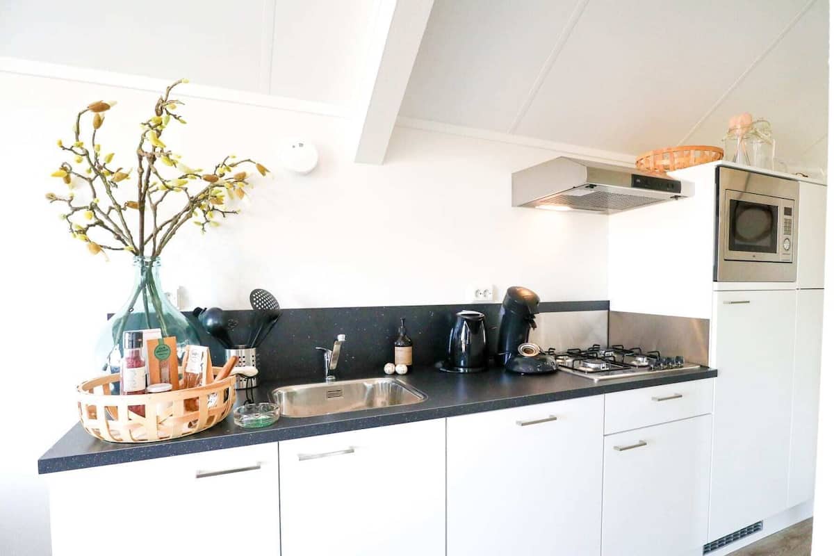 Une cuisine moderne avec des meubles blancs, un plan de travail noir, une cuisinière à gaz, une machine à café et un vase rempli de fleurs.