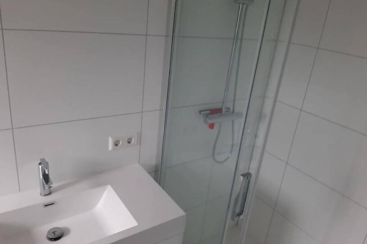 Une salle de bain avec un lavabo blanc, une cabine de douche en verre et des murs carrelés.