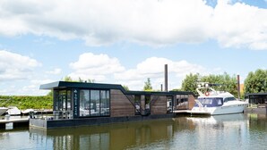 A floating houseboat with a modern design, large windows, and a staircase leading to the upper deck. - Europarcs Marina Strandbad (Olburgen)