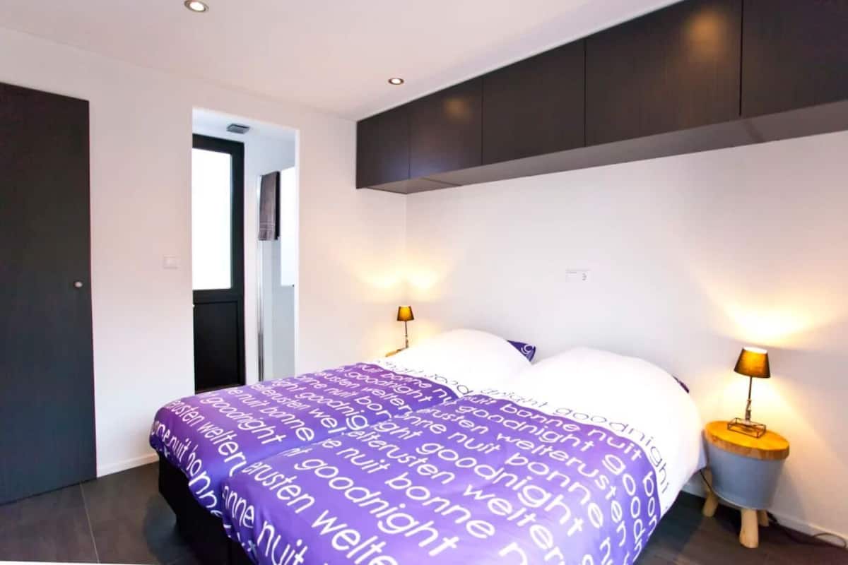 Une chambre à coucher moderne, avec un lit, deux lampes de chevet et une porte donnant sur une autre pièce.