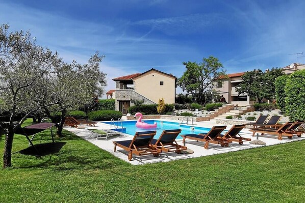 A pool area with lounge chairs, a pink flamingo float, and a building with a red roof.
