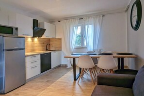 Moderni keittiö, jossa on sisäänrakennettu uuni, mikroaaltouuni ja liesi. Keittiössä on ruokailutila, jossa on pöytä ja tuolit, sekä ikkuna, jossa on verhot.
