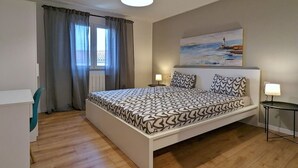 Ein Schlafzimmer mit einem großen Bett, einem Schreibtisch, einem Stuhl, einer Lampe und einem Bild an der Wand.