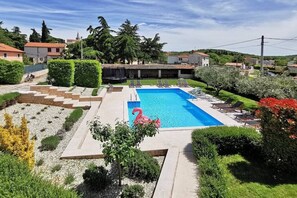 A rectangular swimming pool with a pink flamingo decoration, surrounded by a well-maintained garden with hedges and a small staircase leading to a covered area.