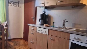 A compact kitchen with wooden cabinets, a built-in dishwasher, a coffee maker, and a sink. - House Severin Whg Findling ground floor (Nieblum)