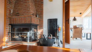 A cozy room with a brick fireplace, a wicker chair, and a wooden table. - Haus Husen - Haushälfte A Heini (Poppenbüll)