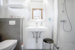 A bathroom with a toilet, sink, mirror, shower, and a stool.