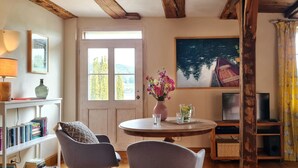 Un salon chaleureux avec une table ronde en bois, deux chaises, une bibliothèque, un téléviseur et un tableau accroché au mur.