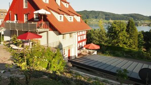 Un chalet rouge et blanc doté d’un balcon, offrant une vue sur un lac et des collines.