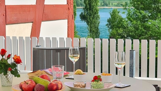 Une table dressée pour un repas, avec des fruits, un verre de vin et une vue sur un lac.